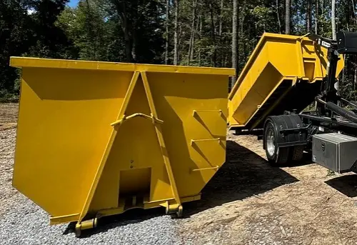 RapidPolk Dumpster Rental unloads a yellow roll-off dumpster beside another container near a wooded area