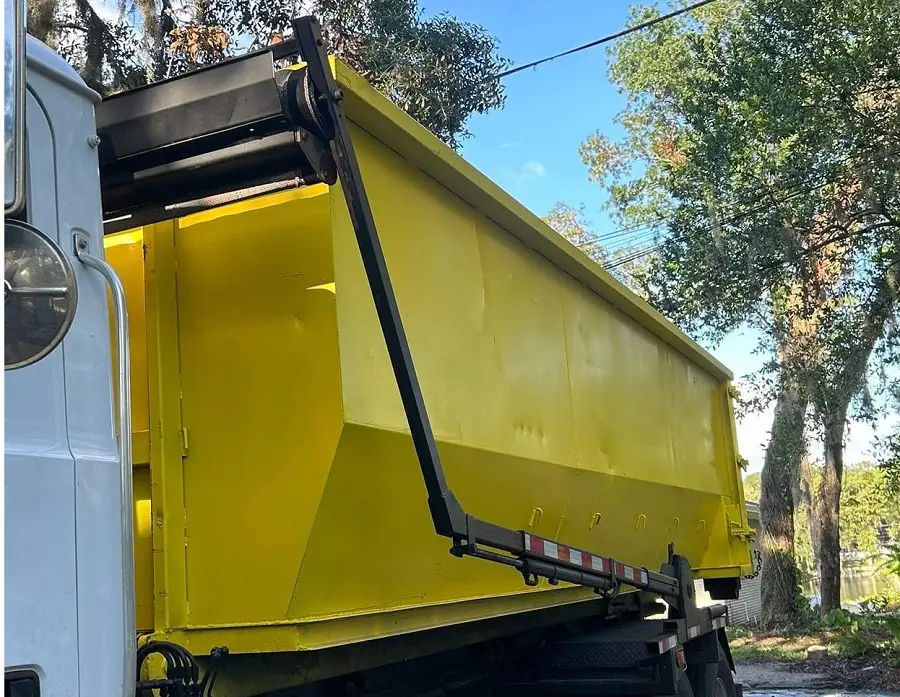 Residential dumpster rental by RapidPolk loads yellow dumpster onto tilt truck in driveway